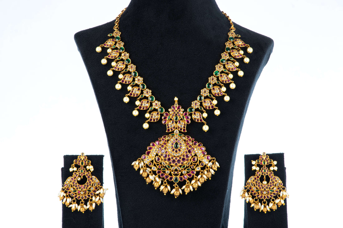 A multi-color polki necklace set with gold plating, pearls, and intricate designs displayed on a black mannequin bust with a pair of matching earrings.