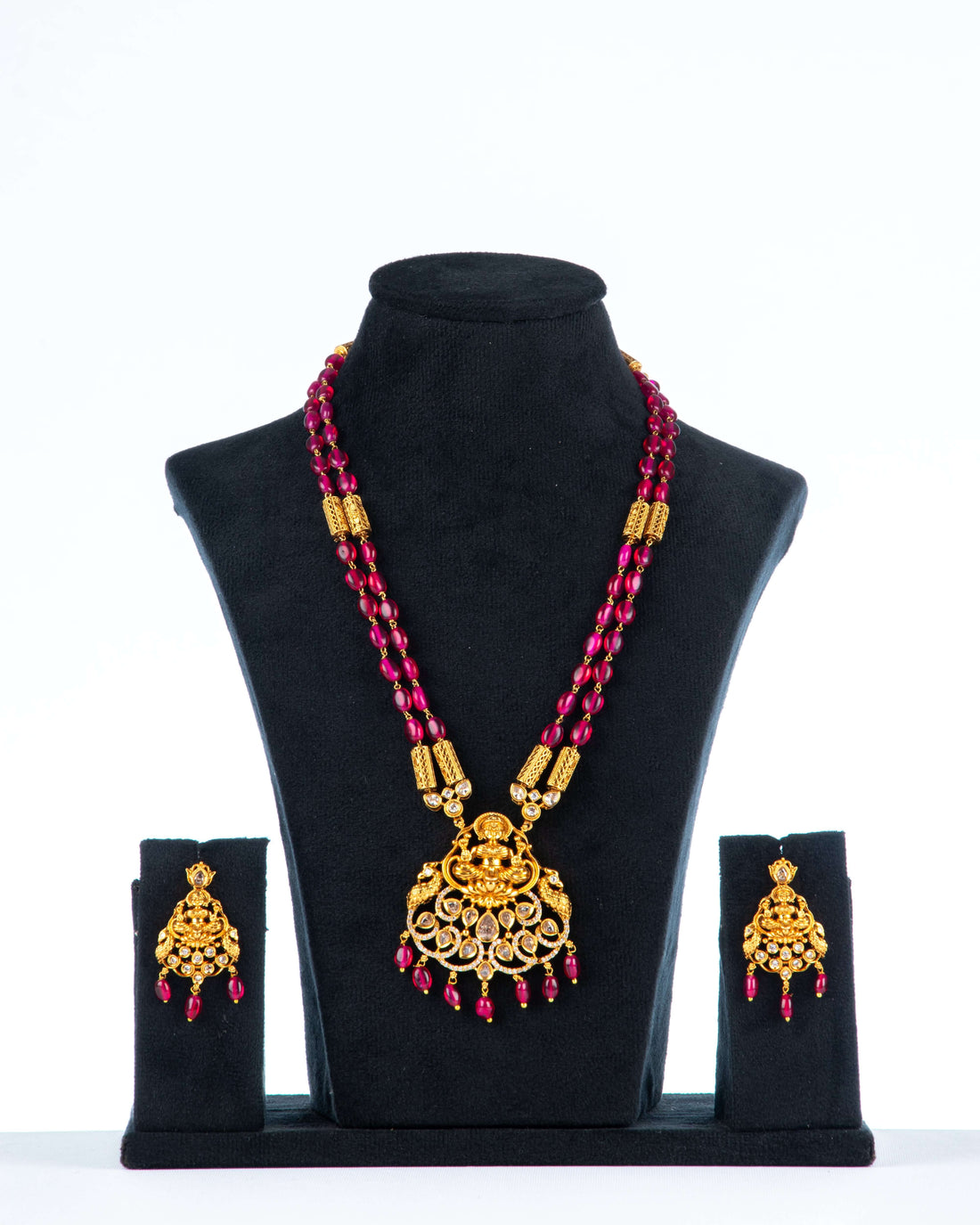 A beaded long necklace set with intricate gold-colored temple jewelry pendant and coordinating earrings, displayed on a mannequin bust.