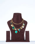A double-layered, chunky agate necklace with a gold-toned chain. The necklace features two large, irregularly shaped teal-colored agate stones as the main pendants. The chain is also decorated with various charms, including white seashells, a starfish, and a sun. The necklace is displayed on a dark brown jewelry bust.