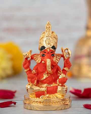 A vibrant red and gold colored statue of Lord Ganesha, seated, wearing a golden crown and ornaments.