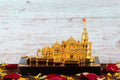 Golden replica of the Ram Mandir temple, surrounded by red and yellow flower petals on a dark base.