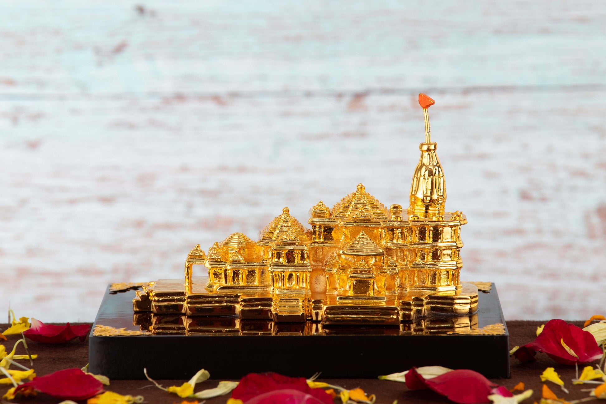 Golden replica of the Ram Mandir temple, surrounded by red and yellow flower petals on a dark base.
