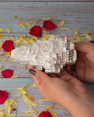 Ayodhya Ram Mandir idol without a base, held in hands, with rose petals scattered on a rustic wooden surface in the background.