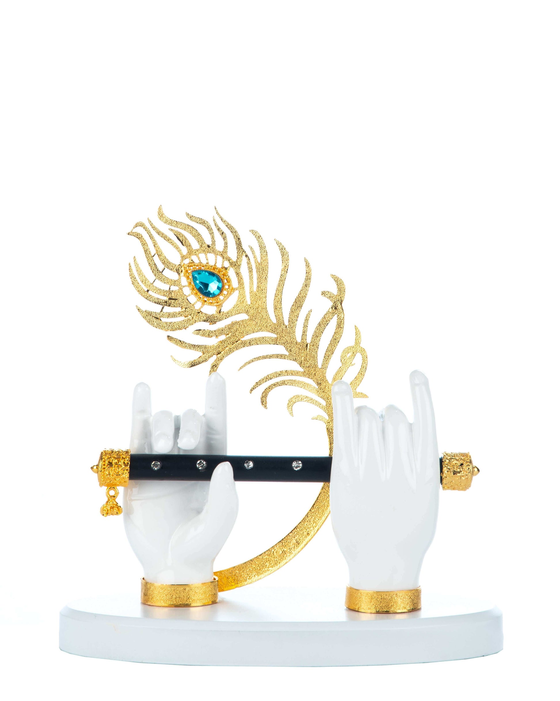 A decorative showpiece featuring two white hands holding a black flute, with a golden peacock feather adorned with a prominent blue jewel behind them, all mounted on a white circular base with golden accents at the wrists and around the flute holders.