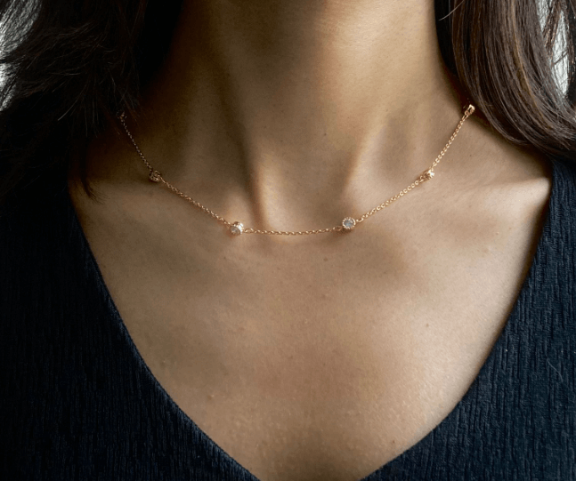 A person wearing a gold-colored Station Chain Necklace with a V-neck top and a sleeveless blue dress.