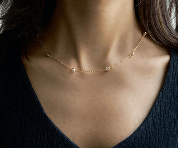 A person wearing a gold-colored Station Chain Necklace with a V-neck top and a sleeveless blue dress.