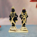 A pair of black statues, depicting the Hindu deities Lord Vitthal and Goddess Rukmini, adorned with golden ornaments and standing on a gold-colored base.