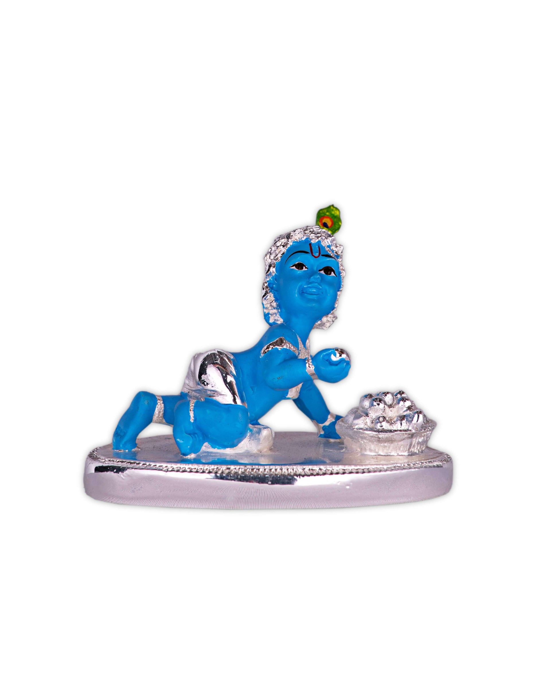 A blue-skinned idol of baby Lord Krishna (Bal Gopal/Laddu Gopal) crawling on a silver-colored base, adorned with a peacock feather on his head and holding a sweet or butter pot.