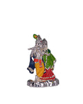 A silver-plated idol of Radha Krishna. Krishna is depicted with a peacock feather in his crown and holding a flute, while Radha stands beside him, both adorned in colorful clothing with intricate details.