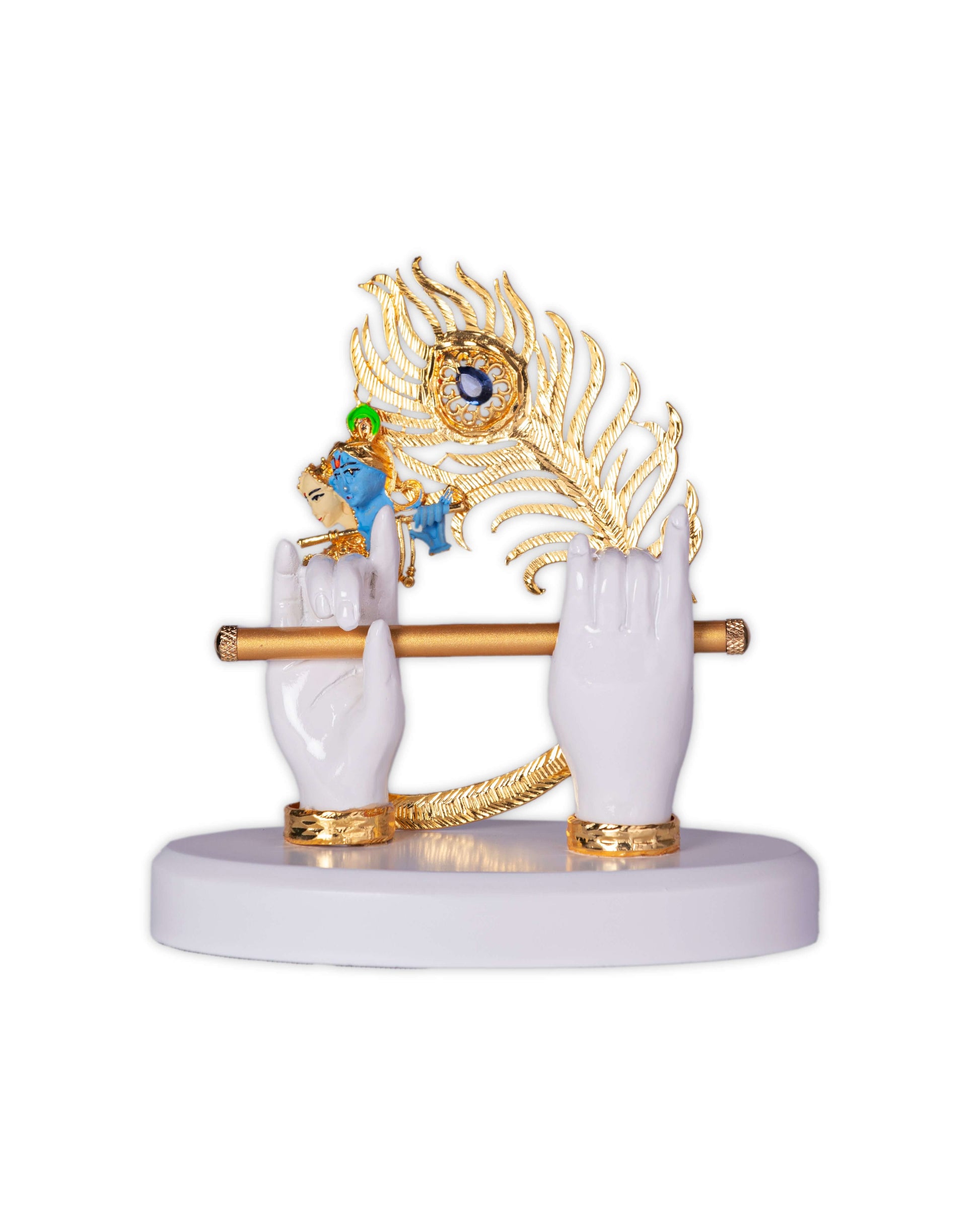 A decorative idol featuring Lord Krishna's white hands holding a golden flute, with a golden peacock feather and a miniature blue figure of Krishna playing the flute on a white base.