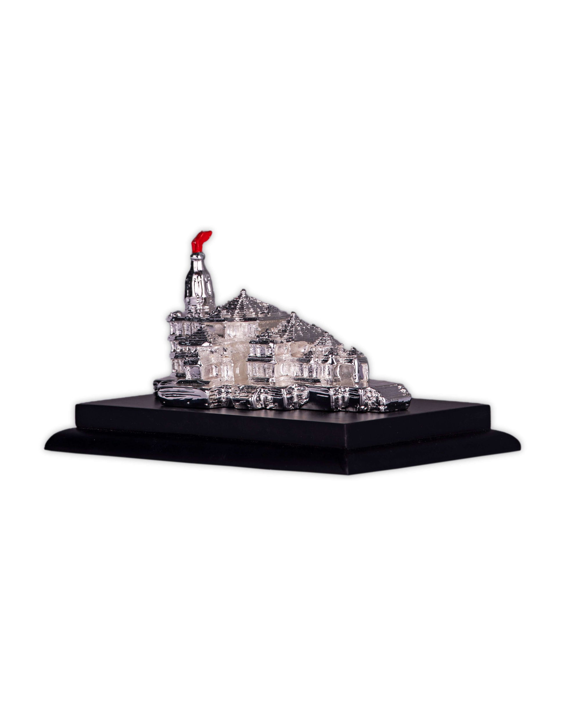 A silver-plated 3D model of the Ayodhya Ram Mandir with intricate detailing, resting on a black rectangular base. A small red flag or banner is visible atop the highest spire of the temple model.