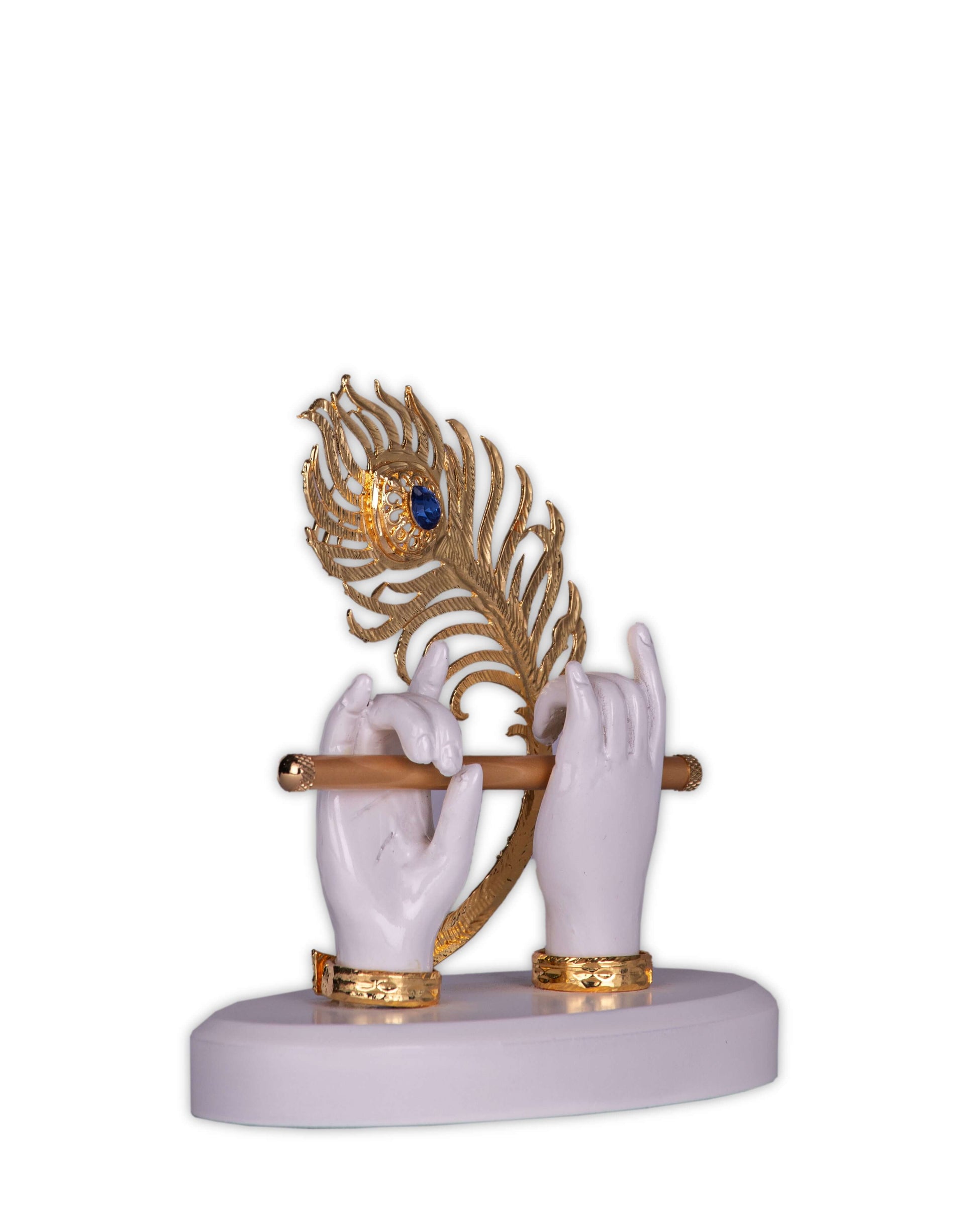 A white and gold sculpture depicting Lord Krishna's hands holding a flute, with a large, elaborate peacock feather adorned with a blue gem behind them, all set on a simple white base.
