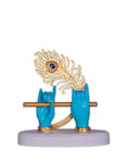 A sculpture featuring Lord Krishna's turquoise-colored hands holding a golden flute, with a vibrant golden peacock feather adorned with a blue gem rising behind them, all resting on a white base.