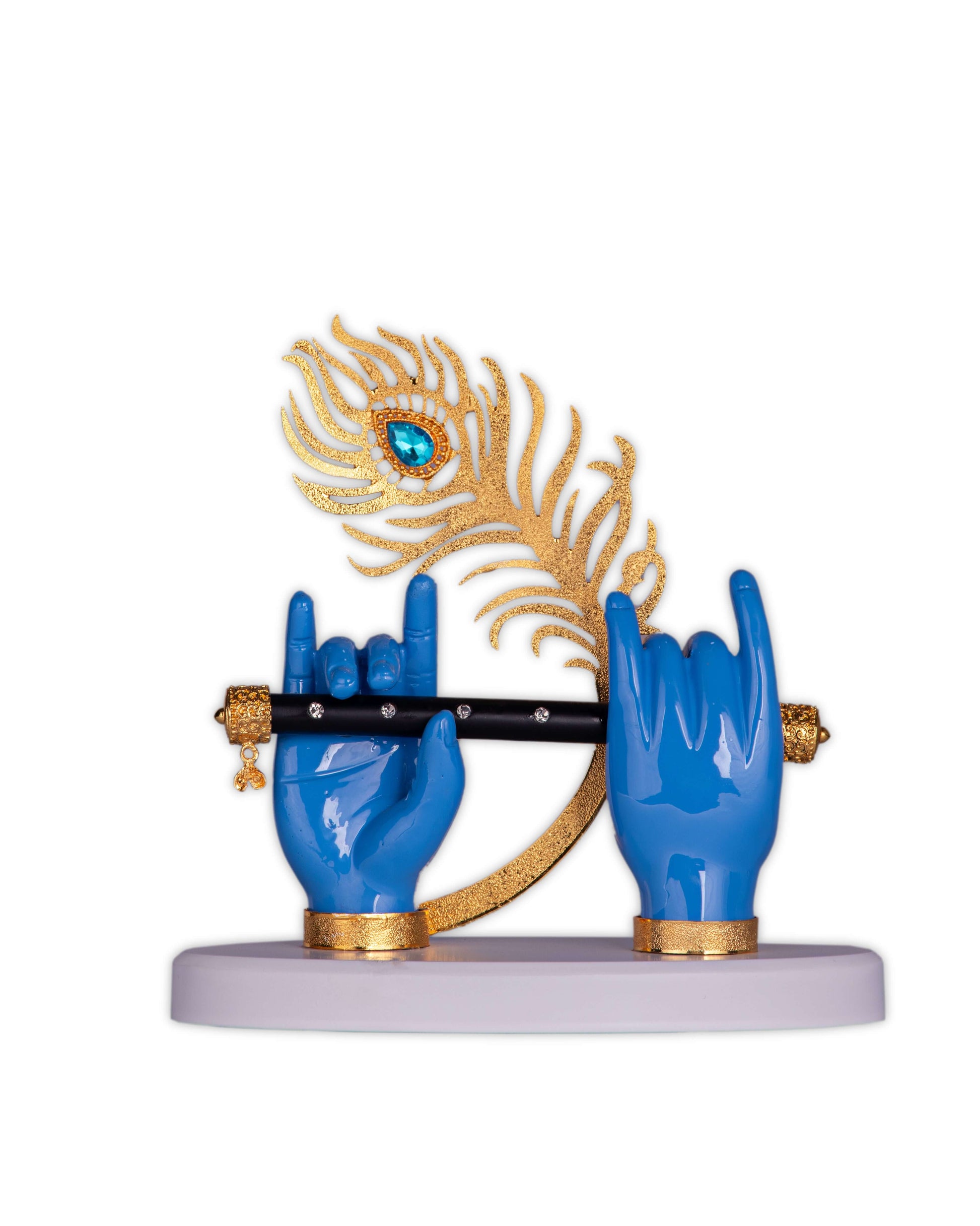 A sculpture featuring two blue hands, typically associated with Lord Krishna, holding a black flute with golden details. Behind the flute and hands is a prominent golden peacock feather adorned with a blue gemstone, all mounted on a light-colored base.