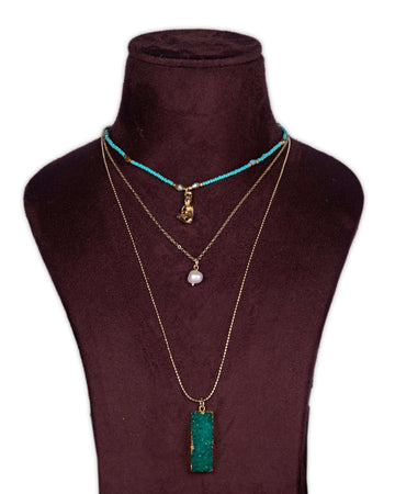 A display of layered necklaces with a prominent green agate pendant as the focus, set on a mannequin bust.