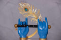 Sculpted blue hands, likely representing Lord Krishna, hold a black flute adorned with small gems, while a large golden peacock feather featuring a prominent blue jewel is positioned behind them.