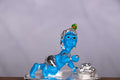 A statue of Bala Krishna (Baby Krishna) crawling, depicted with blue skin, silver-colored clothing, and a peacock feather on his head, with a small pot of butter next to him.