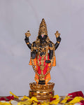 A black and gold-colored idol of Lord Venkateswara, also known as Balaji, adorned with traditional attire and jewelry, standing on a golden lotus base.