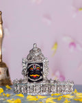 A silver-plated Mahakal idol, a fierce form of Lord Shiva, adorned with intricate details and traditional markings, placed on a surface scattered with yellow flower petals.