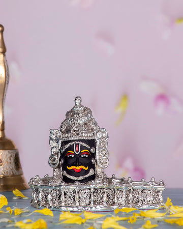 A silver-plated Mahakal idol, a fierce form of Lord Shiva, adorned with intricate details and traditional markings, placed on a surface scattered with yellow flower petals.
