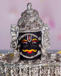 A detailed, close-up shot of a silver-plated idol of Lord Mahakal (Shiva), featuring a dark face with a prominent orange mustache, red tilak, and intricate silver ornamentation including a crown and base.