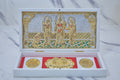 A white box open to reveal a gold-plated Ram Darbar tableau inside, featuring Lord Rama, Sita, Lakshmana, and Hanuman, alongside golden religious coins on a red velvet base.