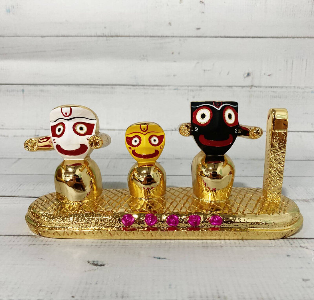 Three gold-plated idols of Lord Jagannath, Lord Balabhadra, and Goddess Subhadra, distinctively depicted with large round eyes and simplified forms, standing side by side on a golden base