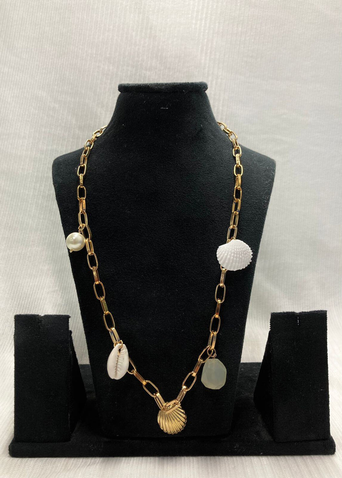 A necklace with gold chain and aqua semi-precious charm shells along with a baroque pearl, displayed on a mannequin.