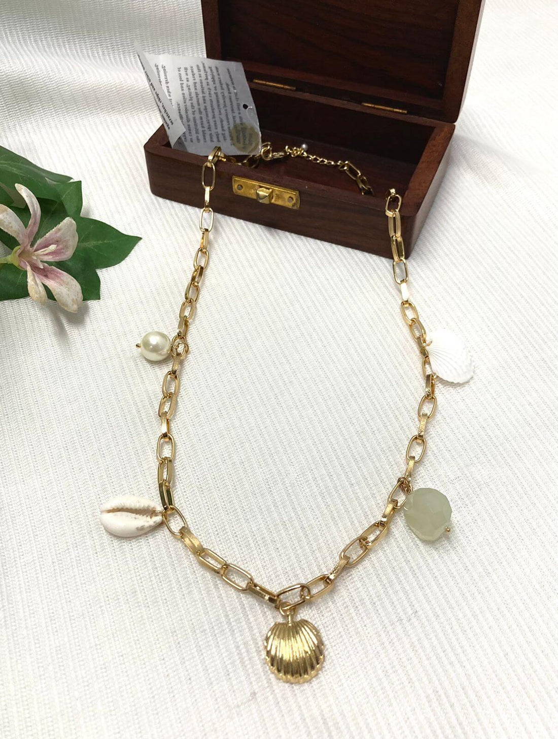 A necklace with gold chain and aqua semi-precious charm shells along with a baroque pearl, displayed on a mannequin.