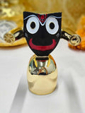 Close-up of a black Lord Jagannath idol with large round white eyes and red facial details, set on a reflective gold-plated base.