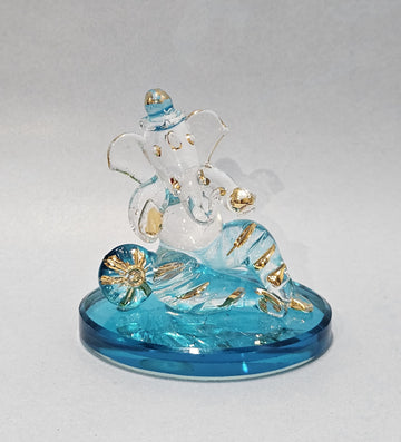 A translucent blue and clear glass Ganesha statue with gold accents, seated on a round blue base.