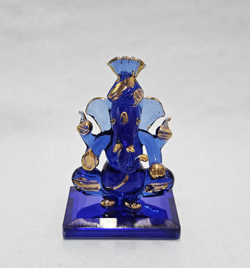 A small, intricately designed blue and gold Pagri Ganesha idol made of glass or crystal, seated on a rectangular blue base.