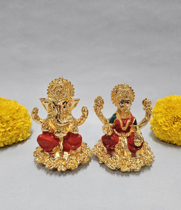 Gold-plated idols of Lord Ganesha and Goddess Lakshmi, seated on lotus-like bases, flanked by vibrant yellow marigold flowers on a light background.