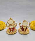 Gold-plated idols of Lakshmi and Ganesha adorned with yellow marigold flowers on a light background.