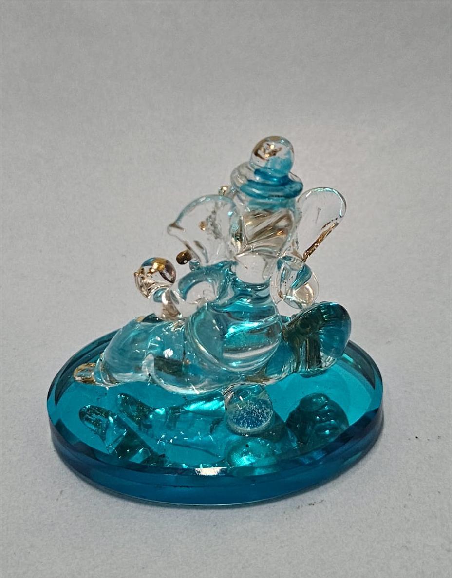 A clear and blue-tinted crystal or glass idol of Lord Ganesha seated on a vibrant blue base.