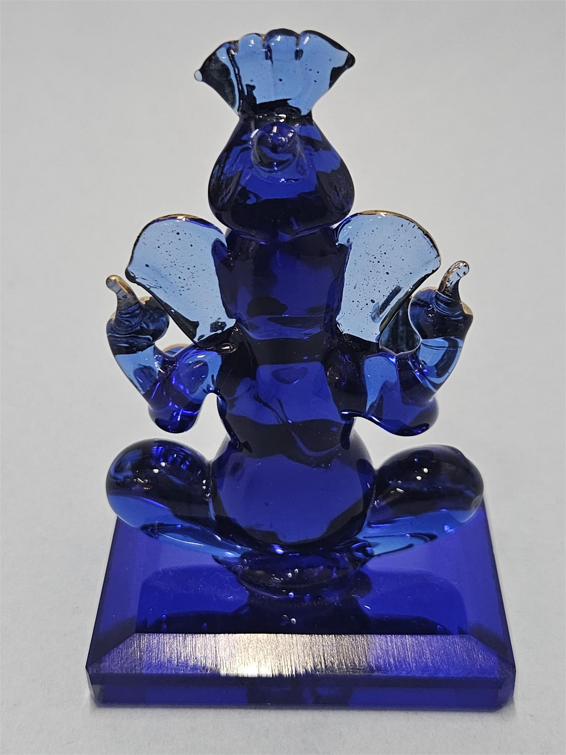 A blue glass statue of the Hindu deity Ganesha, shown seated on a rectangular base.