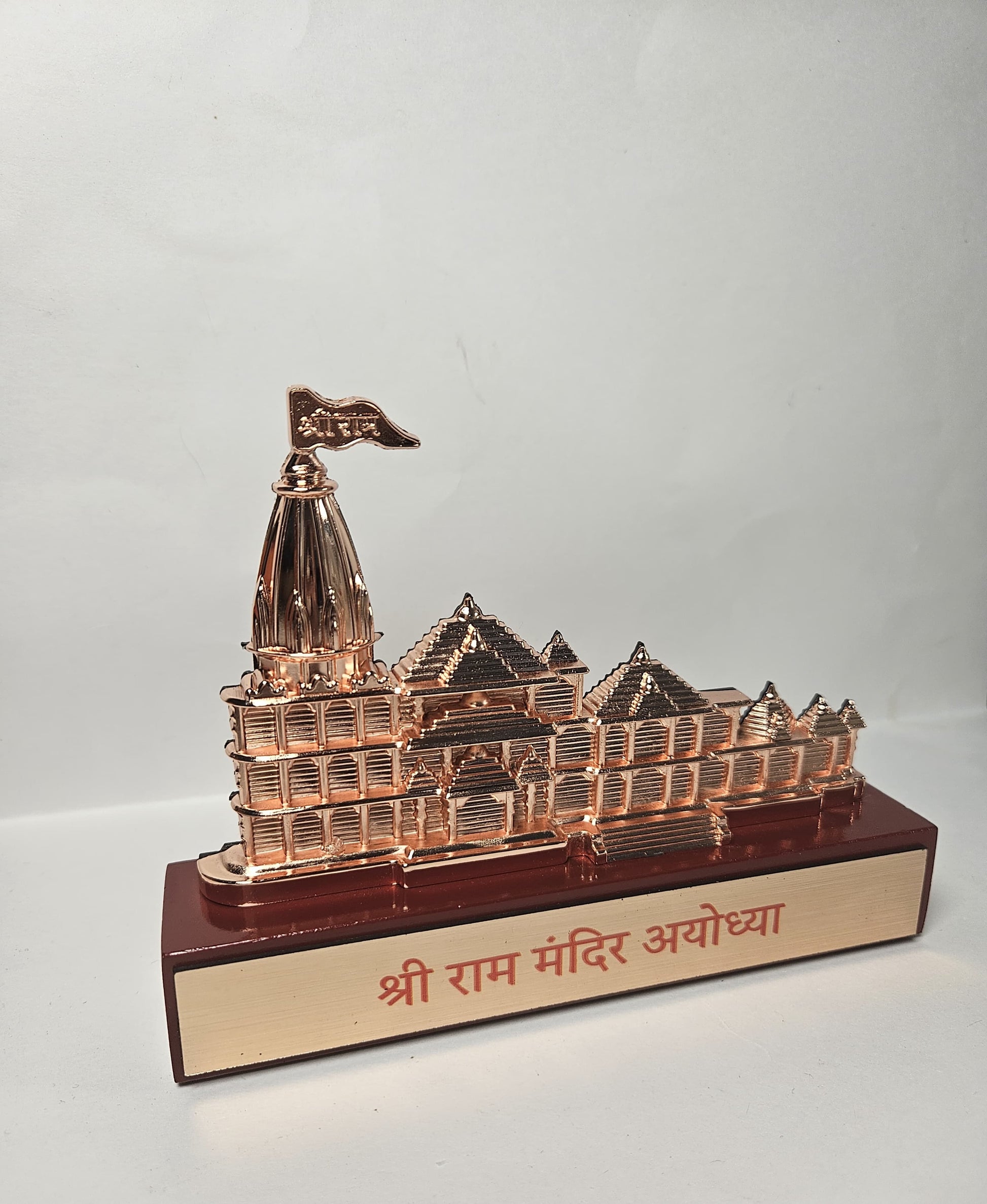Rose gold metallic idol of the Ram Mandir Ayodhya, a spiritual souvenir or decorative piece, on a brown rectangular base with Hindi script.
