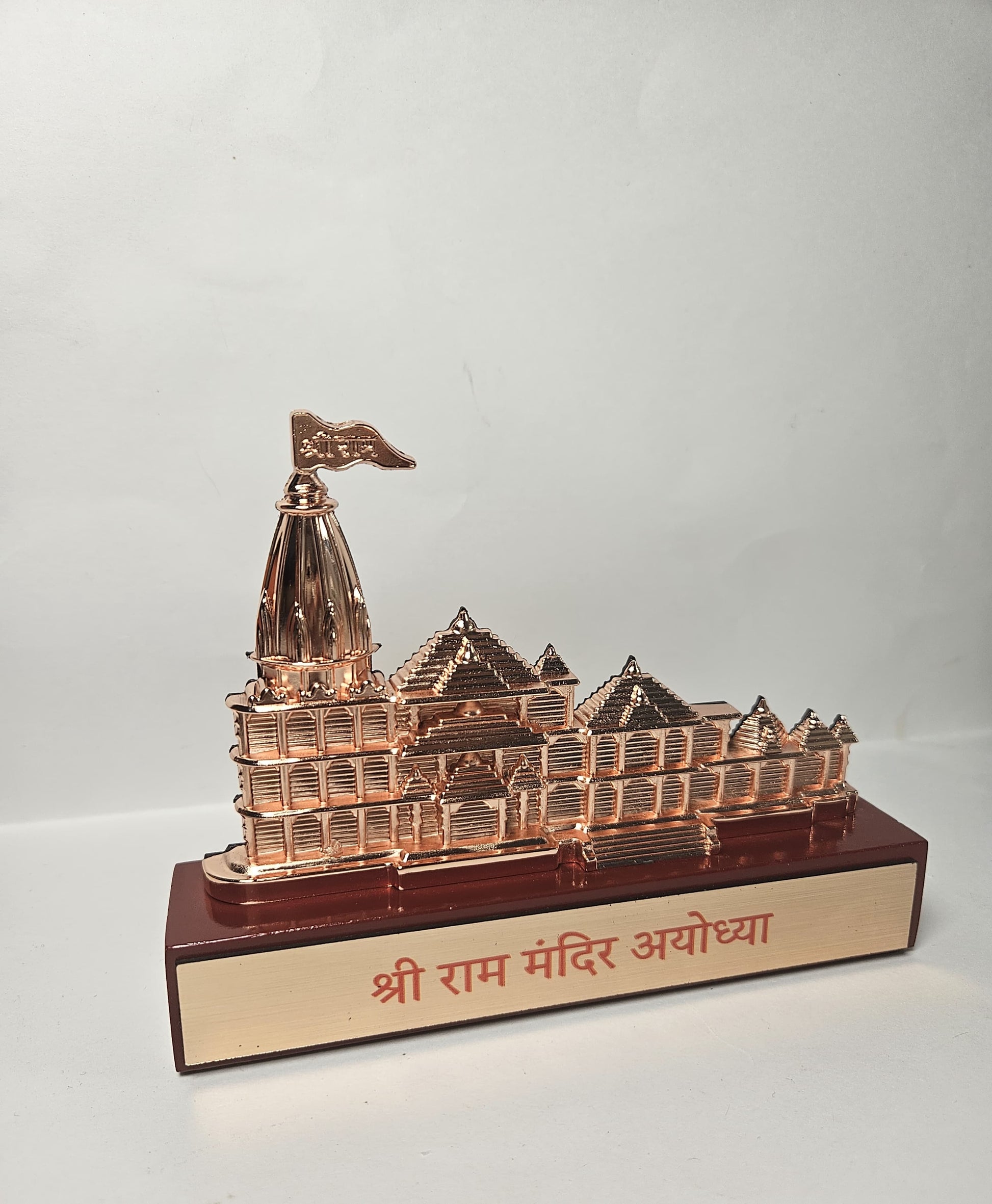 A detailed, rose gold-colored miniature idol of the Ram Mandir temple in Ayodhya, placed on a dark red base with 'श्री राम मंदिर अयोध्या' inscribed in Hindi.