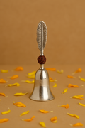 Metal bell with feather design on a brown background with yellow petals.