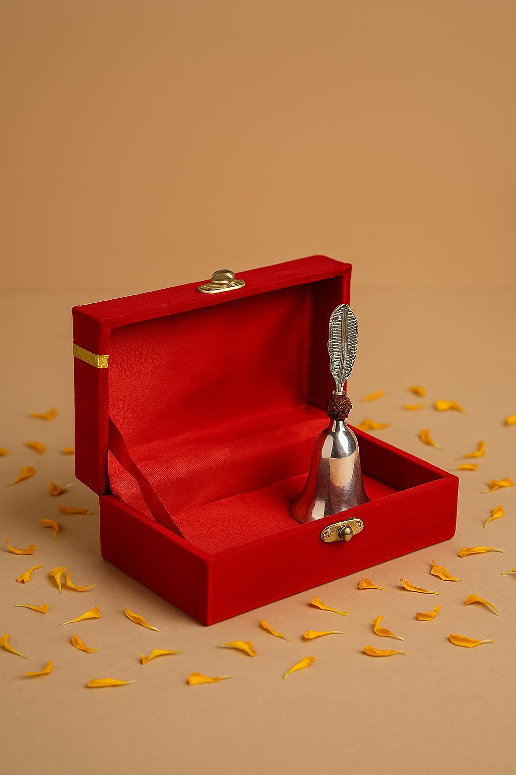 Silver bell with a string in a open red box on a beige background with yellow leaves.
