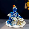 A blue idol of Bal Krishna playing a silver flute while sitting next to a silver cow.