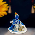 A blue figurine of Bal Krishna playing a silver flute, seated beside a silver cow.