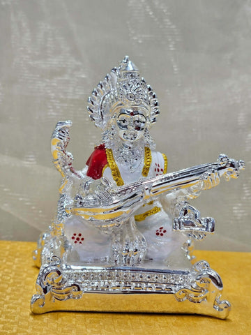 A detailed silver-plated idol of Goddess Saraswati, depicted seated and gracefully playing a veena, with intricate detailing on her attire and ornamentation.
