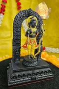 A black and gold polyresin statue of Ram Lalla Idol from Ayodhya, depicting a child Lord Rama holding a bow and arrow, standing within an intricately carved black archway on a multi-tiered base, against a soft yellow background.