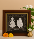 A wooden-framed silver idol featuring Goddess Lakshmi and Lord Ganesha sitting on lotus pedestals, with