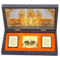 A dark wooden box containing a gold-plated Ram Darbar set. Inside, Lord Rama, Sita, Lakshman, and Hanuman are depicted, with Charan Padukas (divine footprints) placed in the center. Two gold-framed plaques with Sanskrit text are also visible on the inner lid.