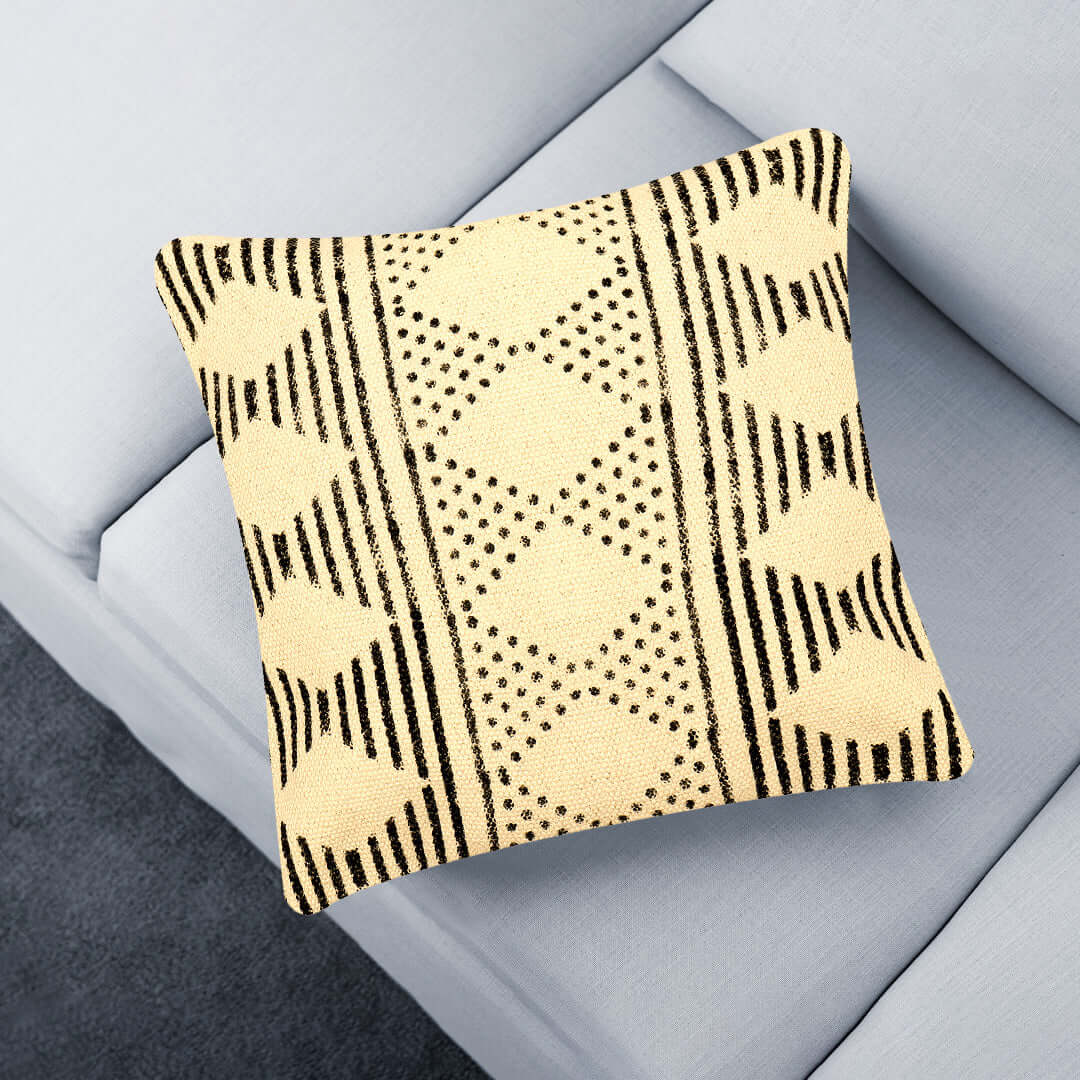 A beige and black tribal motif pillow cover on a gray sofa.