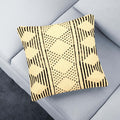 A beige and black tribal motif pillow cover on a gray sofa.