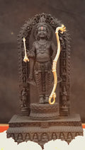A dark-hued idol of Ram Lalla, the child form of Lord Rama, crafted from Krishna Shila (black granite), holding a golden bow and arrow, adorned with jewelry, and standing on a lotus pedestal within a carved archway.