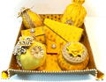 A collection of bridal trousseau gift set including metal boxes, bangles, and other wedding accessories, predominantly in yellow and adorned with decorative elements.